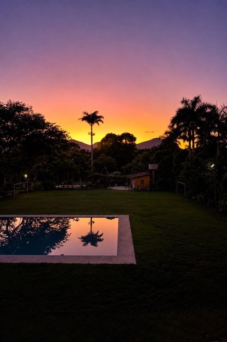 O sítio ao amanhecer, com o céu alaranjado refletido na piscina